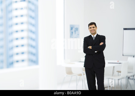 Geschäftsmann, stehend im Büro mit Armen gefaltet, lächelnd in die Kamera Stockfoto