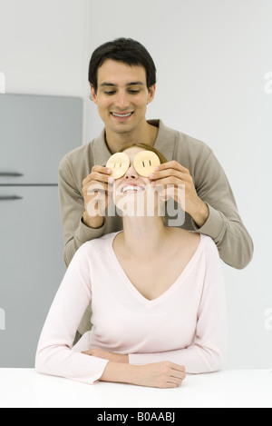 Junges Paar in der Küche, Mann, hält FRUCHTSCHEIBEN vor den Augen Frau Stockfoto