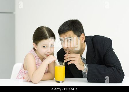 Kleine Mädchen und Vater trinken aus Glas Saft mit einem Strohhalm, Blick in die Kamera Stockfoto