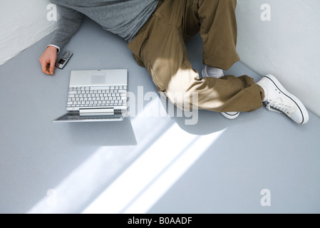 Junger Mann sitzt auf dem Boden vor Laptopcomputer, beschnitten Ansicht Stockfoto