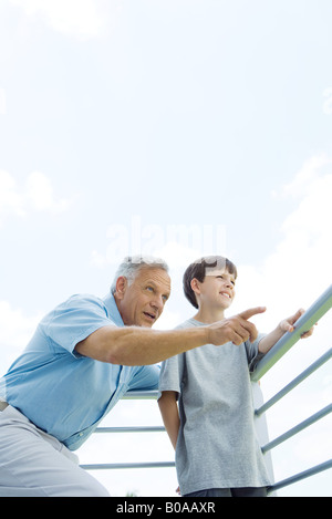Mann mit Arm um Enkels Schulter stehend, zeigt, beide suchen Weg, niedrigen Winkel Ansicht Stockfoto