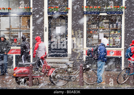 Amsterdam, Nieuwezijds Voorburgwal Straße in fallenden Schnee, Shop mit Tulpen, Fußgänger, Fahrräder Stockfoto