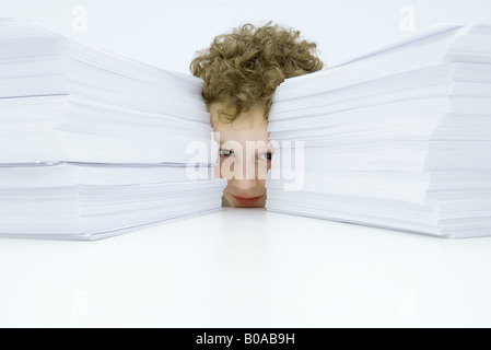 Kleiner Junge hinter zwei großen Stapel von Papier, in die Kamera guckend Stockfoto