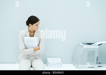 Junge Frau im Anzug sitzt neben Drucker Stockfoto