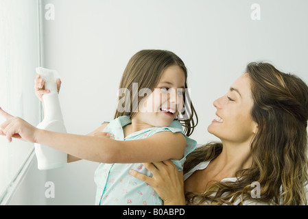 Kleines Mädchen Reinigung Fenster zeigen, Mutter lächelte Stockfoto