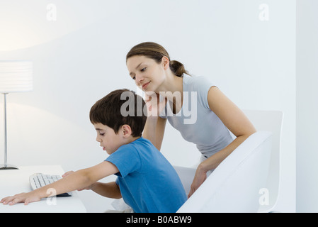 Kleiner Junge mit Computer-Tastatur, Mutter wacht über seine Schulter Stockfoto