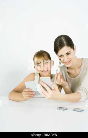 Junge Frau sitzt neben preteen Schwester, setzen auf Make-up, beide auf der Suche in die Hand Spiegel Stockfoto