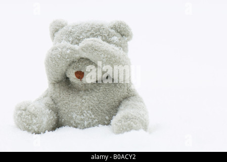 Teddy Bär sitzen im Schnee, seine Augen mit den Händen bedecken Stockfoto