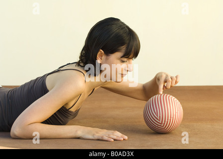 Frau liegend auf Bauch, berührt Ball mit Finger, Seitenansicht Stockfoto