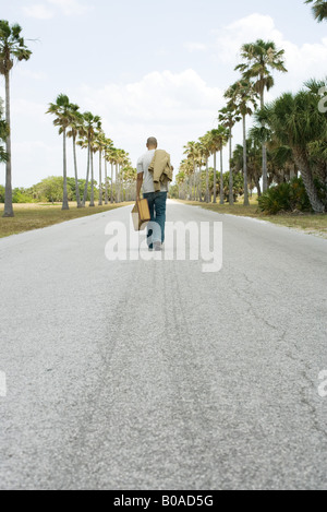 Mann zu Fuß in der Mitte der Straße, mit Koffer und Jacke, Rückansicht Stockfoto