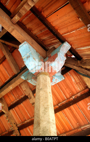 Geschnitzte Steinsäule, die Unterstützung von Holzbalken und Ziegeldach eines traditionellen Kerala-Haus Stockfoto