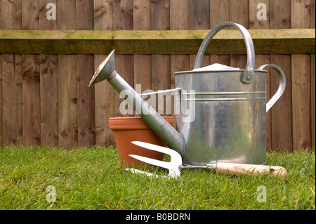 Stillleben mit einer Gießkanne Hand Gabel und Terrakotta-Topf auf dem Rasen im Garten Stockfoto