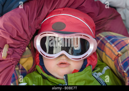 Ein einjähriges Mädchen Ski Brille liegt in einem Buggy, gut geschützt vor Kälte Stockfoto