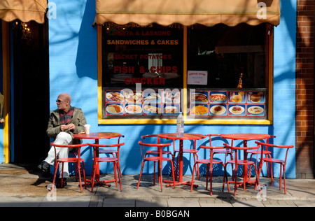 Mann sitzt im roten Metall-Tisch und Stühle auf Bürgersteig vor der blauen und gelben Café, Marchmont Street, Bloomsbury, London, England Stockfoto