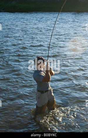 Ein Fliegenfischer kämpft einen großen Fisch beim Fliegenfischen auf Forellen. Stockfoto