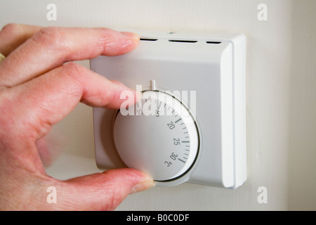 Rentner von Hand drehen nach unten Home zentrale Heizung Thermostat bei niedriger Temperatur ein Haushalt Energiekosten und CO2-Ausstoß zu reduzieren. England Großbritannien Stockfoto