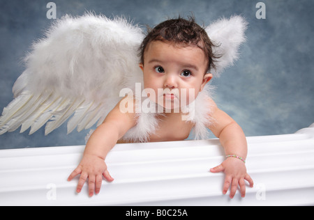 Hispanischen Mädchen tragen Engelsflügel Klettern auf einer weißen Säule in einem Porträtstudio Stockfoto