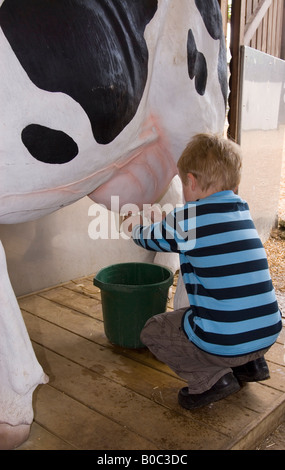 Kleiner Junge Melken Modell Kuh an der Junior-Farm in Wroxham Scheunen In Norfolk, Großbritannien Stockfoto