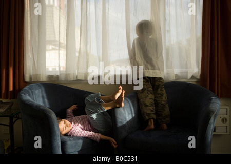 Junge im Alter von sechs blickt Fenster Mädchen im Alter von vier Jahren sitzt im Sessel Motelzimmer Wellington New Zealand Stockfoto