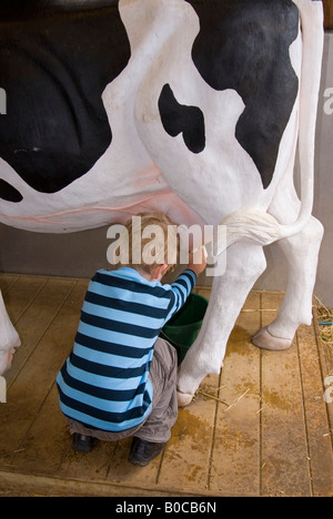 Kleiner Junge Melken Modell Kuh an der Junior-Farm in Wroxham Scheunen In Norfolk, Großbritannien Stockfoto