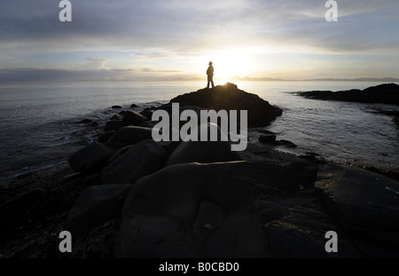 EINE PERSON UHREN EINEN DRAMATISCHEN SONNENUNTERGANG AN DER KÜSTE VON KINTYRE BLICK AUF DER ISLE OF JURA, SCHOTTLAND, VEREINIGTES KÖNIGREICH. Stockfoto