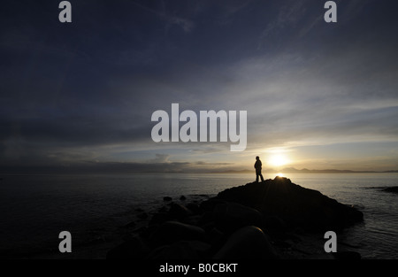 EINE PERSON UHREN EINEN DRAMATISCHEN SONNENUNTERGANG AN DER KÜSTE VON KINTYRE BLICK AUF DER ISLE OF JURA, SCHOTTLAND, VEREINIGTES KÖNIGREICH. Stockfoto