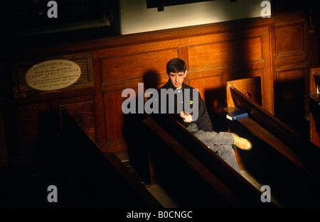 Eine junge gefährdeten aussehenden Jugendlichen sitzt allein besorgt und in isolierten Filterung Sonne auf eine kirchliche Bank in Wesley Chapel London Stockfoto