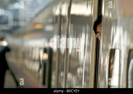 Dirigent peering Fromn ein Fenster von einem Shinkansen "Bullet Train", zu trainieren, da es weg von Tokio JR-Bahnhof, Japan zieht Stockfoto