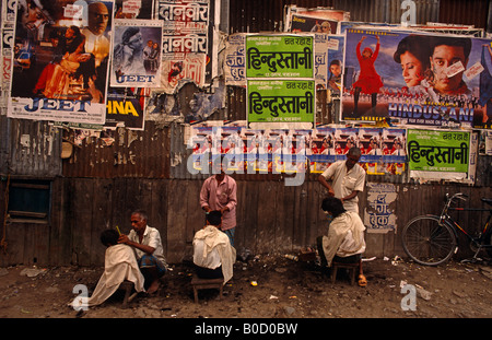 Outdoor-Friseure schneiden Kunden Haare in einer Calcutta Straße mit heroischen Bollywood Movie Poster an Wand hinter Stockfoto