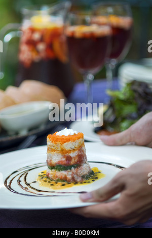 Hände liefern einen leckeren Teller mit Krabben Timbale, Salat mit Vinaigrette und roten Wein Sangria auf ein Essen im Freien in Spanien Tische Stockfoto