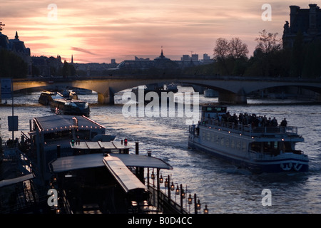 Ausflugsboote bei Sonnenuntergang am Ufer und Musée d ' Orsay und Grand Palais in der Silhouette. Blick auf die Brücke Caroussel Stockfoto