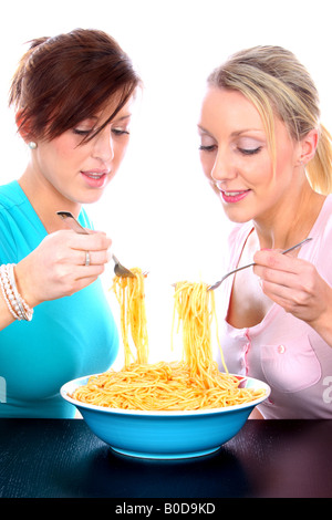 Zwei Freundinnen Teilen und genießen eine große Schüssel mit italienischen Spaghetti Pasta Essen gegen einen weißen Hintergrund isoliert Stockfoto