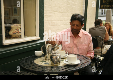 Man gießt Milch in eine Tasse Kaffee in die schiefe Haus Windsor Stockfoto