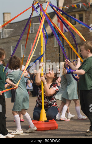 May Day Fair, ein Schullehrer aus dem Dorf der Grundschule hält das Maypole für Kinder aufrecht und hält es ruhig, während sie im Maypole Cambridgeshire UK tanzen Stockfoto