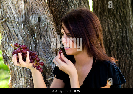 Eine schöne junge Frau, die von Bäumen im Freien sitzen Weintraube in der Hand hält und ein Essen bereitet. Oklahoma, USA. Stockfoto