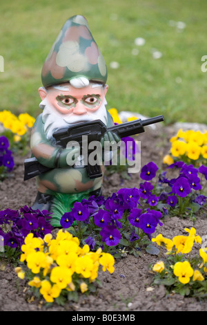 Gartenzwerg in Camouflage mit Maschinengewehr hinter Blumen Stockfoto