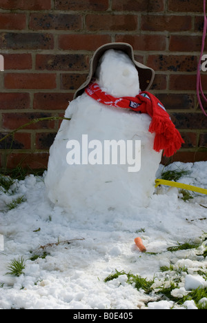 Schneemann mit Nase am Boden trägt einen Hut und roten Schal im Garten Stockfoto