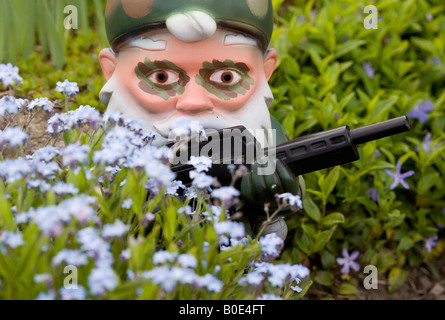 Gartenzwerg in Camouflage mit Maschinengewehr hinter Blumen Stockfoto