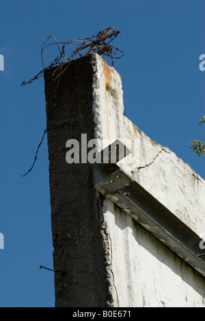 alte Mauer mit alten Metallarbeiten und rostigen Stacheldraht obendrauf vor einem tiefblauen Himmel Stockfoto