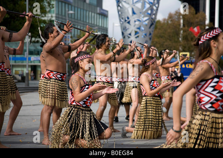 Junge Maori-Frauen und -Männer singen und tanzen in traditioneller Tracht auf dem Cathedral Square, Christchurch, Südinsel, Neuseeland Stockfoto