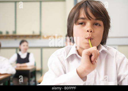 Junge mit Bleistift im Mund, im Klassenzimmer Stockfoto