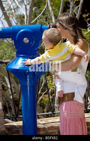 Mutter Holding Kleinkind Blick aber Teleskop an einem Aussichtspunkt in Mijas Pueblo, Costa Del Sol, Andalusien, Spanien Stockfoto