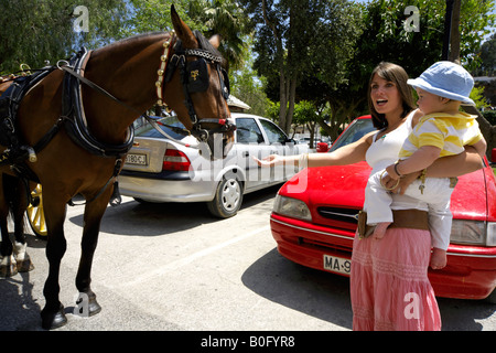 Mutter Holding Kleinkind erreichen, ihre Hand zu einem Schlaganfall-Pferd in den Straßen in Mijas Pueblo, Costa Del Sol, Andalusien, Spai Stockfoto