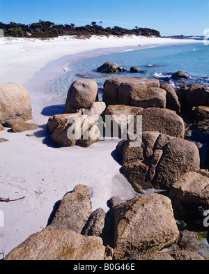 Weißer Sandstrand mit blauem Wasser und ein blauer Himmel mit Felsen im Vordergrund Stockfoto