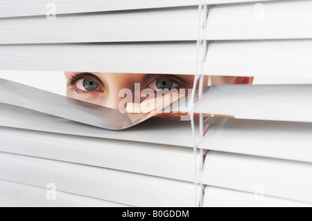 Frau schaut durch Jalousien Stockfoto