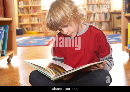 Junge liest ein Buch auf dem Boden Stockfoto