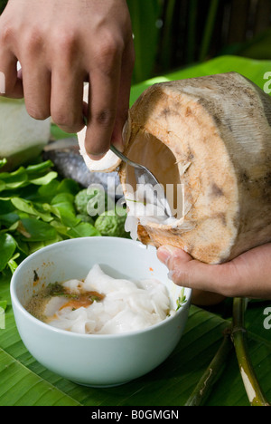 Ein Koch kratzt frische Kokosnuss Fleisch aus der Schale. Dieses natürliche Fleisch ist wichtig in Desserts und Thai-Küche. Stockfoto