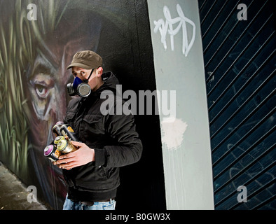 Graffiti-Künstler mit Maske malt spray ein Wandbild an der Wand Stockfoto