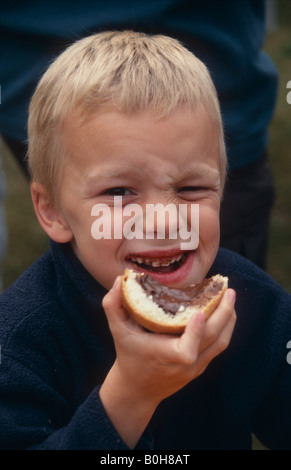 6-jähriger Junge, der eine Scheibe Brot mit Nutella, Schokoladenaufstrich isst Stockfoto