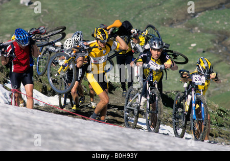 Mountainbiker schieben und tragen ihre Räder durch den Schnee während der Transalp-Challenge am Pfunderer Joch, Bozen-Boze Stockfoto